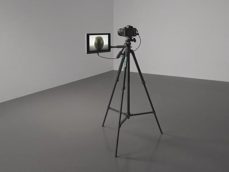 Illustration: Kamera am Stativ neben Monitor mit unscharfem Produktbild im neutralen Studio